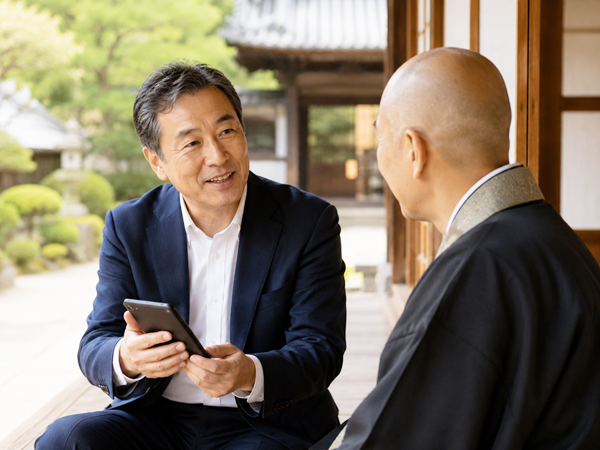 寺院の縁側で住職の相談を受ける男性スタッフ